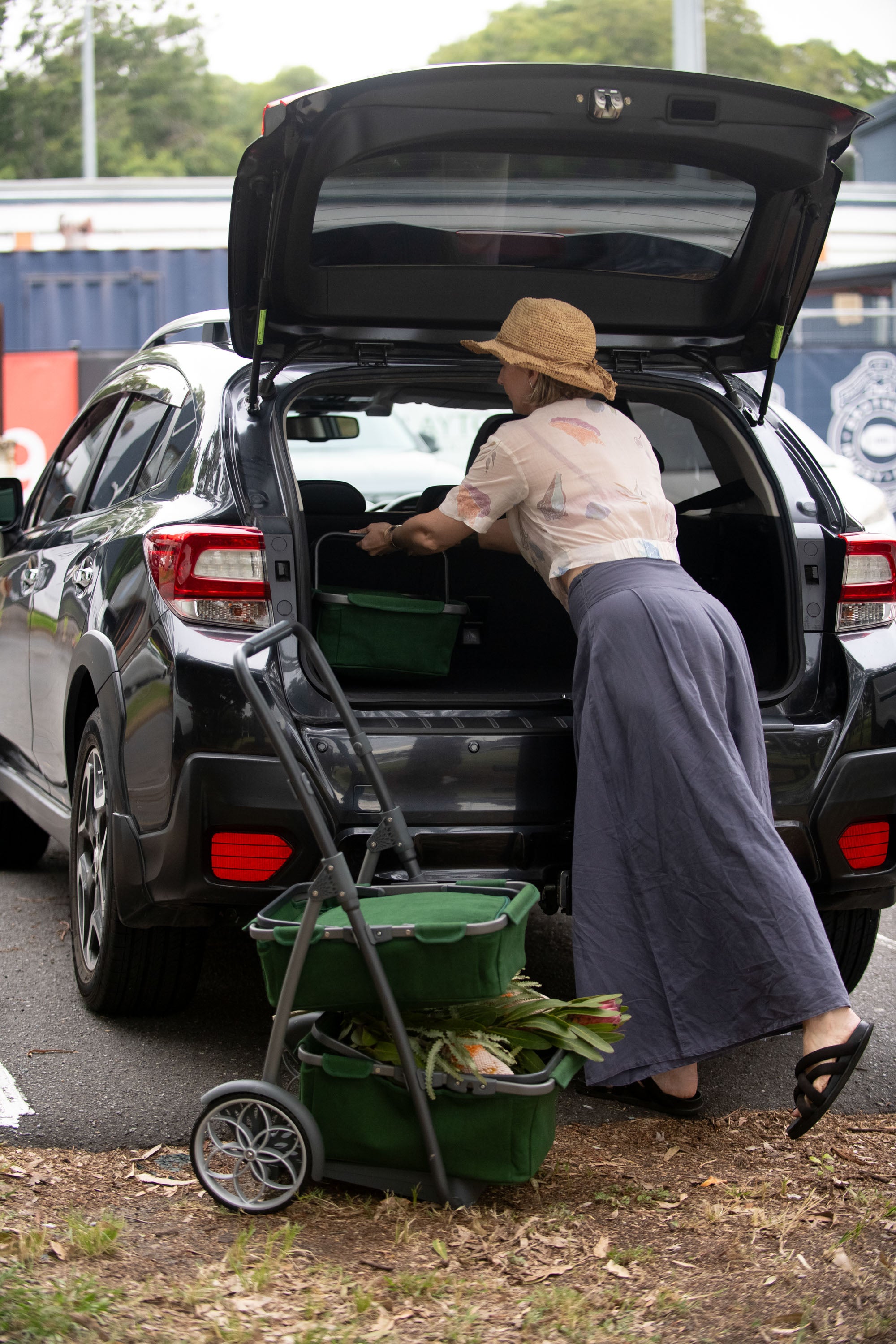 Woman loading groceries into a car trunk with a marketday cart.